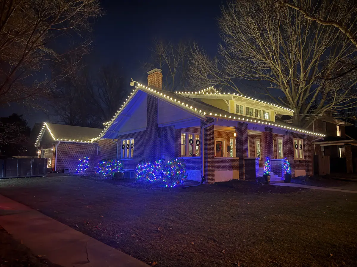 A two-story home with a warm white roofline and blue accent lighting through the yard
